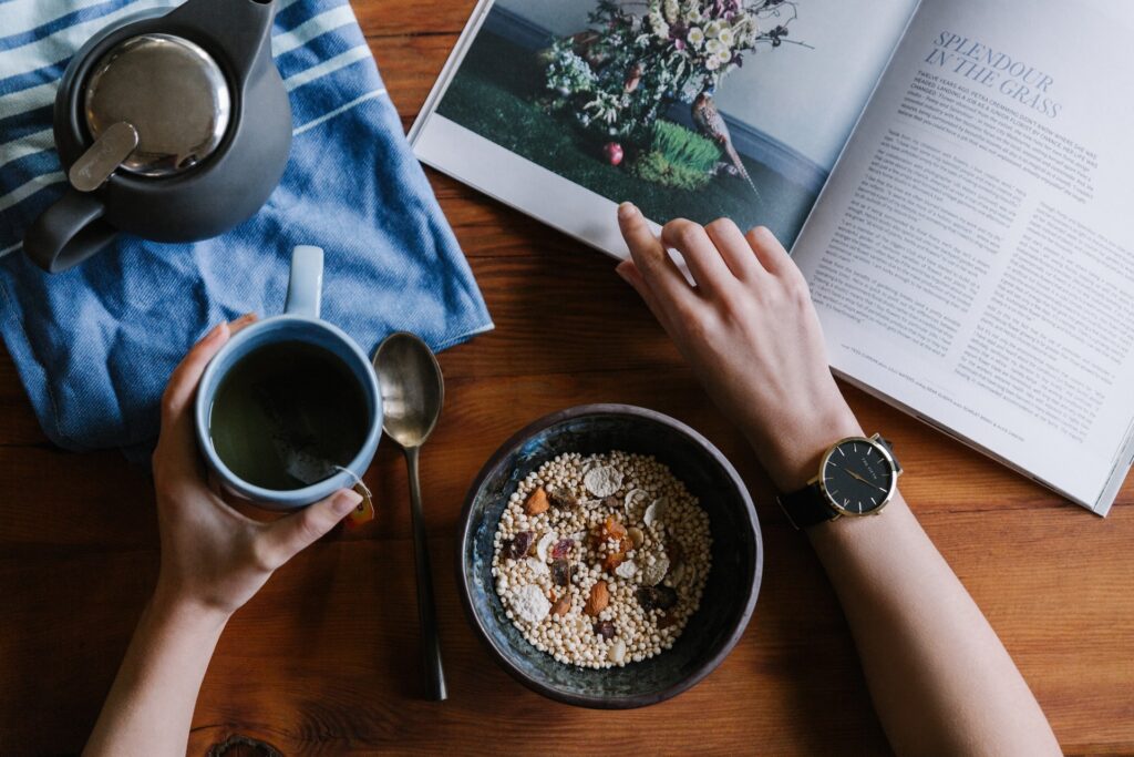 a wooden table with a mug of tea, some muesli and a magazine