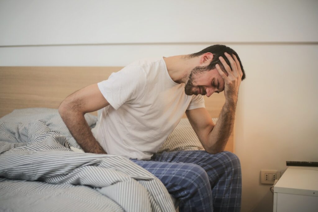 Sleep and Mental Health | Man in early 30s sitting on the side of his bed in PJs, with his head in this hand
