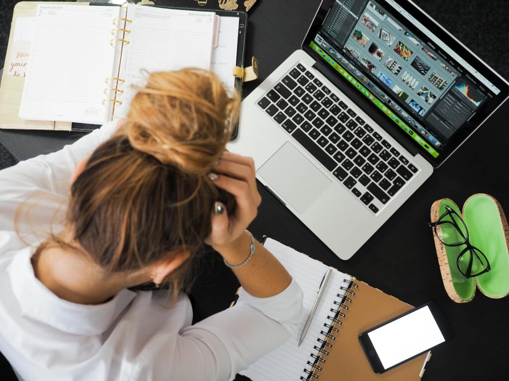 Woman with a messy bun working at laptop with head in hands