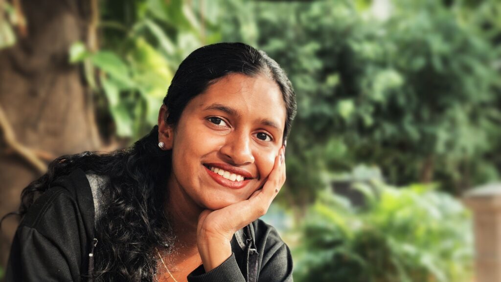 Woman of Indian heritage smiling, sat in nature | 7 Daily Practices to Build Resilience